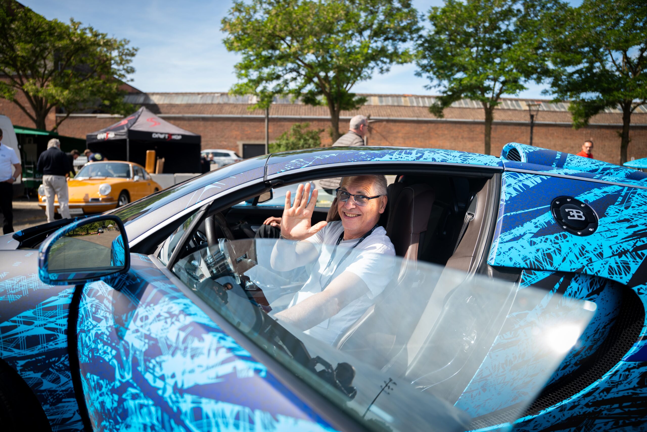 Sportwagen Erlebnisreisen: Glücklicher Teilnehmer winkt aus einem blauen Bugatti Cabrio während der Tour.