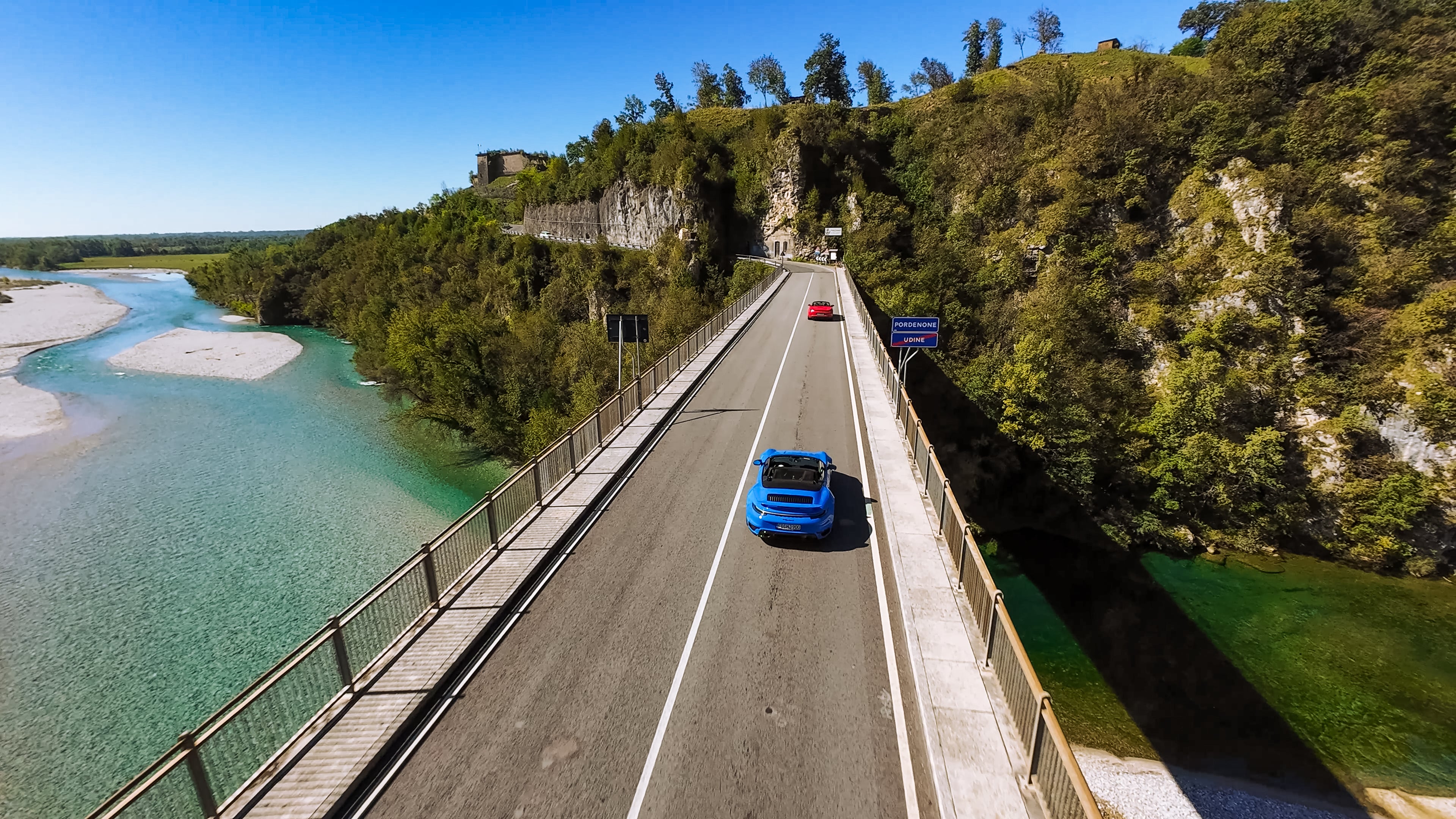 Sportwagen Erlebnisreisen: Blauer Porsche 911 Cabrio überquert eine Brücke über den türkisblauen Fluss.